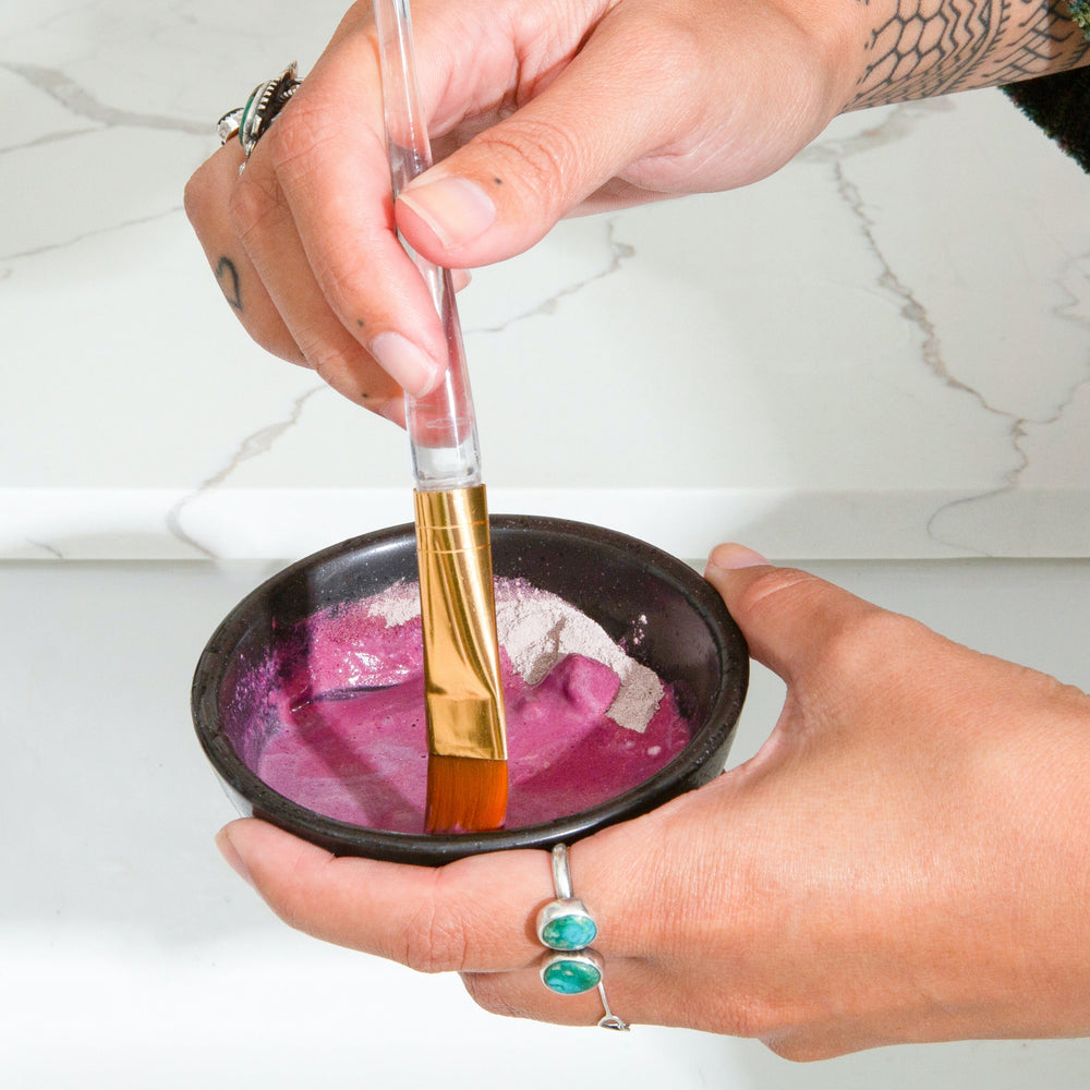 Closeup of Canary Bentonite Clay + Rose Face Mask being mixed with water using a facial brush in a small bowl